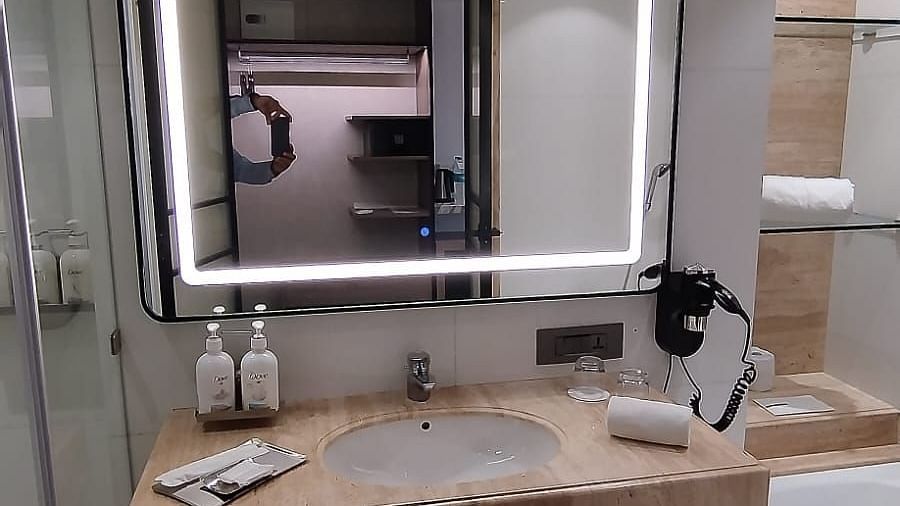 Interiors of a modern bathroom in an executive room at Mirage Hotel, featuring the sink area, an illuminated mirror and a ceramic bathtub.
