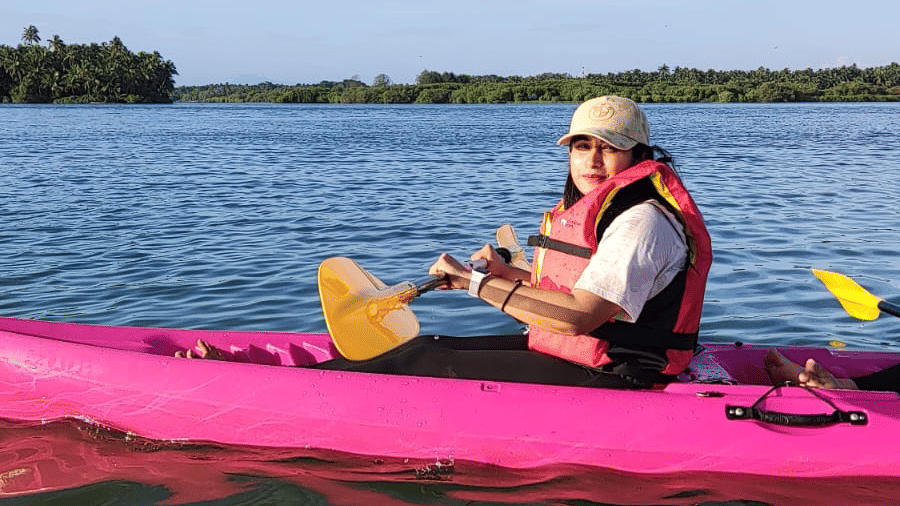 One person in life jackets kayaking in a bright pink kayak on a calm river with distant land in the background at Paradise Lagoon Resort, Udupi.