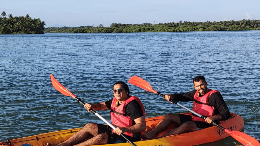 Two people in orange life jackets paddling an orange kayak on a calm river under a clear blue sky at Paradise Lagoon Resort, Udupi.