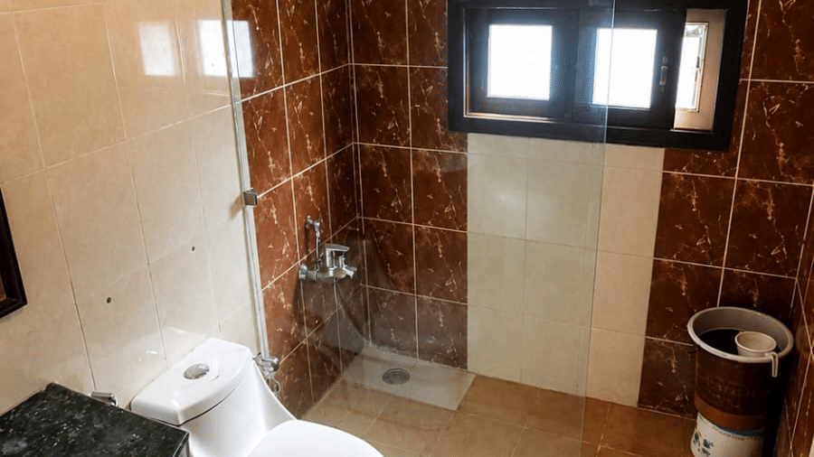 A bathroom at Hotel Outlook, Pahalgam, showing a toilet, a sink vanity basin, wall tiles, and a small window under an overhead light fixture.