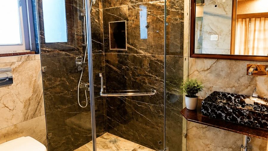 A bathroom at Hotel Outlook, Pahalgam, featuring a glass shower enclosure, a toilet, patterned flooring and a mirror above a vanity unit.