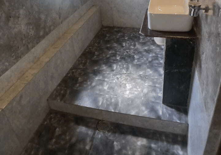 An interior view of a bathroom at Hotel Outlook, Pahalgam, featuring a toilet, tiled flooring, a window, and a glass partition for the shower.