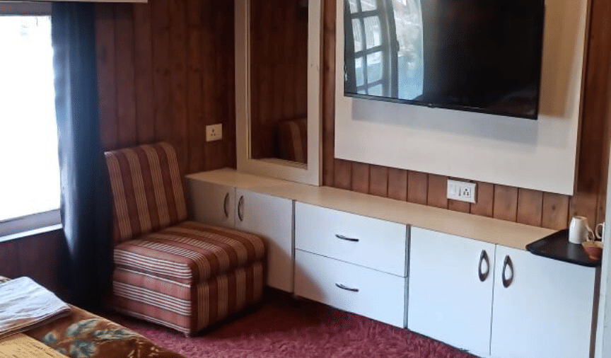 A guest bedroom at Hotel Outlook, Pahalgam, showing 1 double bed positioned against a wood-panelled wall next to a carpeted floor.