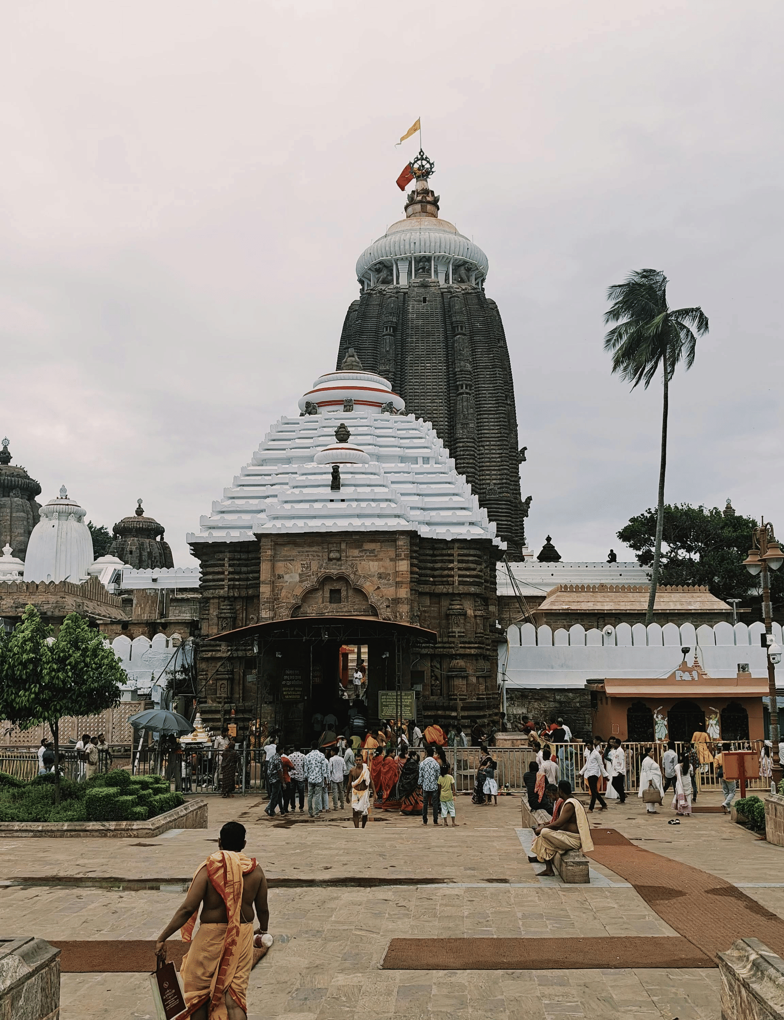 People walking towards a temple with a large dome under a cloudy sky.
