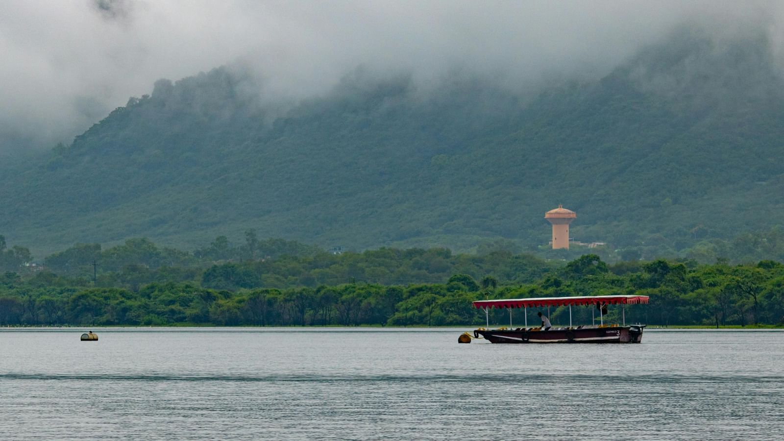 Overview of Fateh Sagar Lake featuring a boat, with mountains in the background partially covered by clouds.