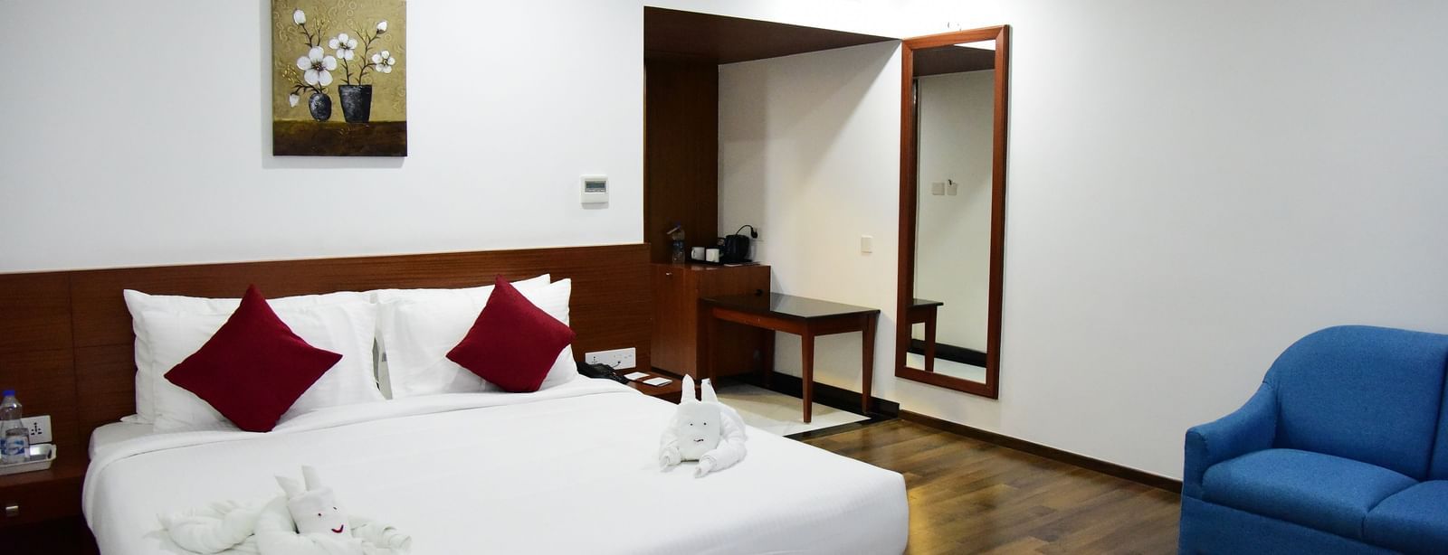 A bright and modern studio room at The Royal Comfort, featuring a comfortable bed with white linens and a stylish teal runner, along with a sleek workspace.