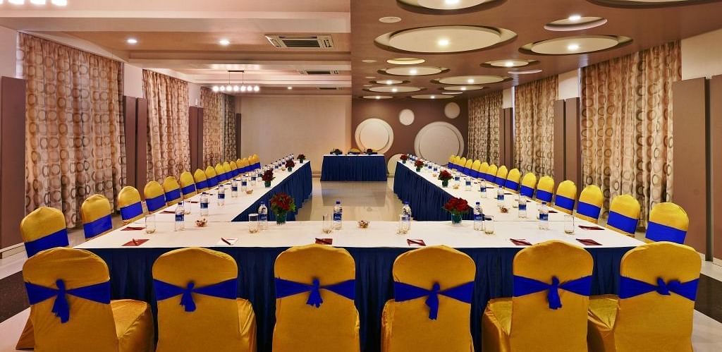 A formal meeting room setup at Lords Inn Porbandar, with a U-shaped table and chairs adorned with blue and yellow sashes.