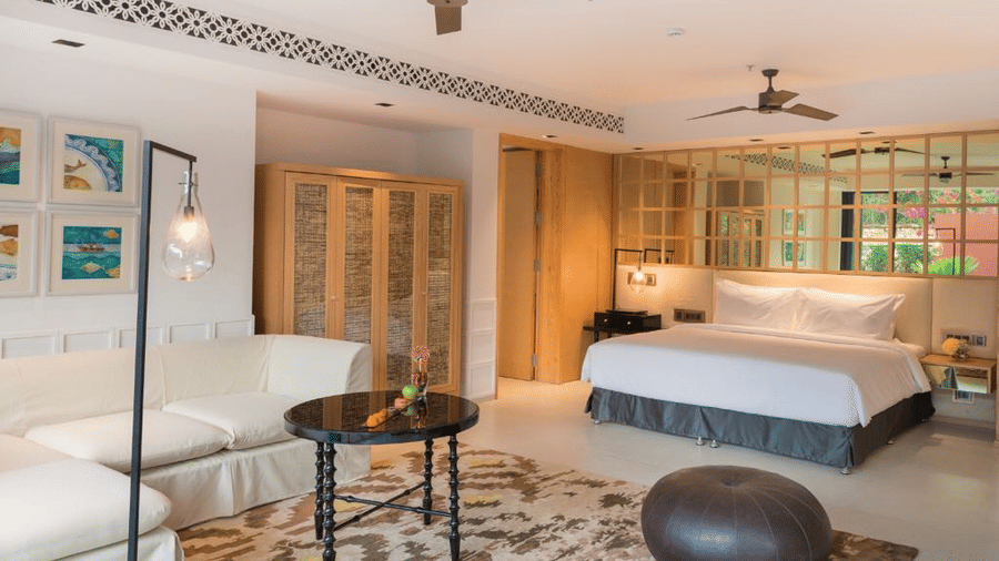 Room with a brown pouffe and a coffee table surrounded by a white couch in front of a plush bed at Azaya Beach Resort Goa