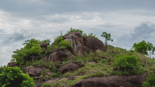 A picturesque green hill with trees and rocky formations under a cloudy sky