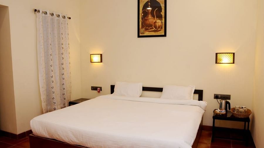 A simple bedroom with white linens, wall sconces, and light beige walls.