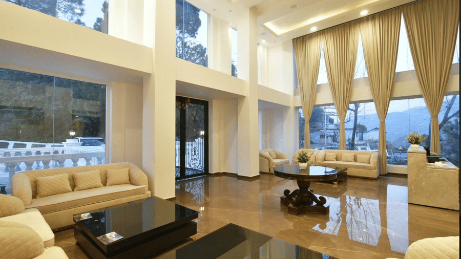 Spacious hotel lobby with tall ceilings, large windows, and comfortable beige seating, filled with natural light.