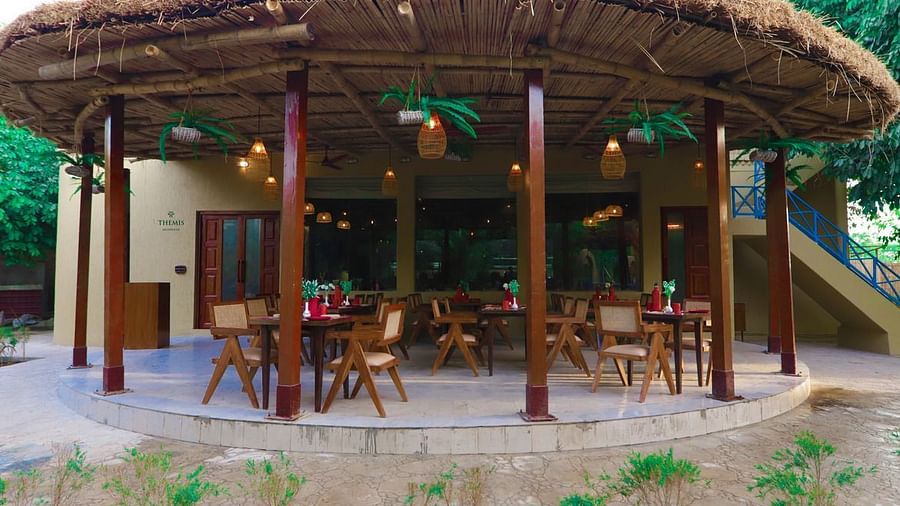 a closeup view of an outdoor restaurant with thatched roof and wooden seats at Themis Mudhouse - A Nature's Retreat Resort & Wellness