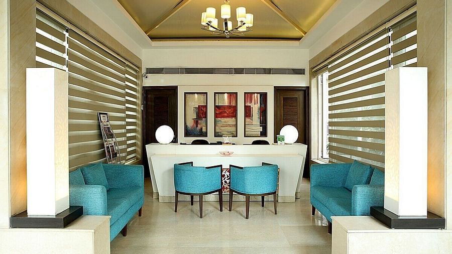 A reception area featuring stylishly arranged furniture, wall-mounted photographs, and a chandelier hanging from the ceiling at Inde Signature Tower, Gurgaon
