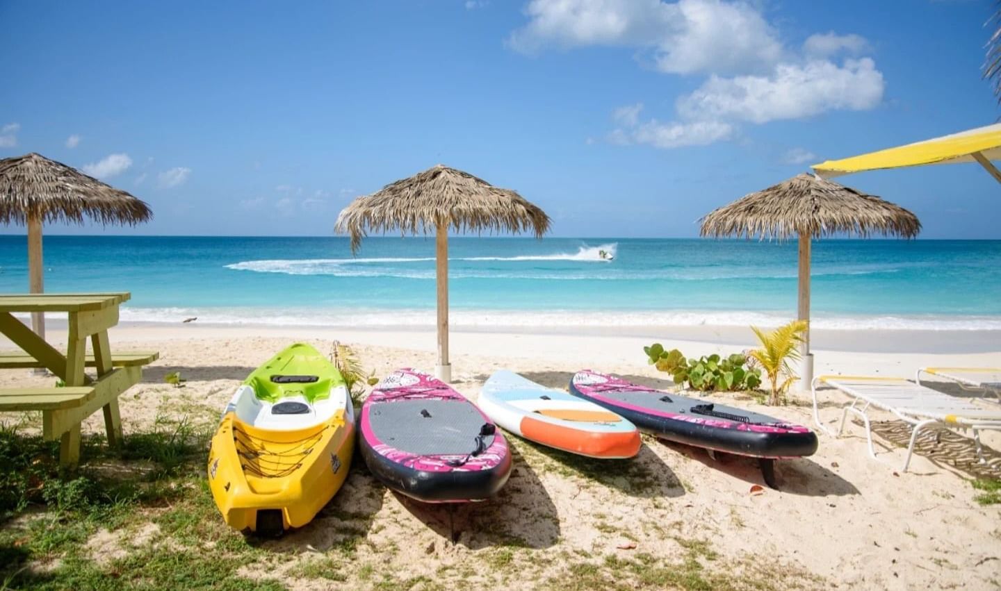 Colourful kayaks lined up on a sunlit Caribbean beach with straw parasols and clear blue skies - Tamarind Hills Resort and Villas - Antigua