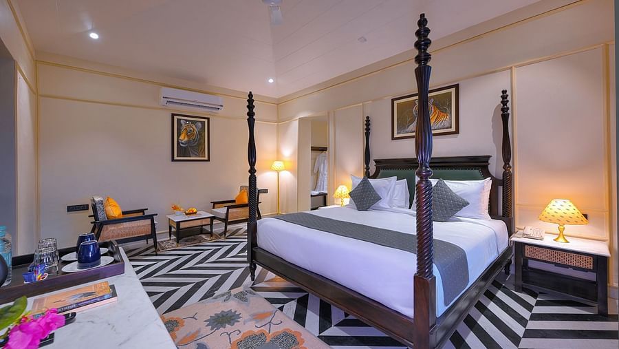 Luxury Suite Cottage with a dark wood four-poster bed, a seating area with orange-cushioned chairs, patterned flooring, and framed artwork - Singhvilas, Ranthambore