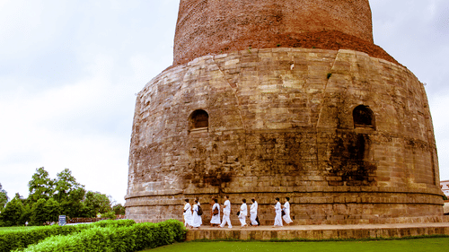 The Dhamek Stupa in Sarnath, Varanasi, with a group of people in white robes standing at its base. 