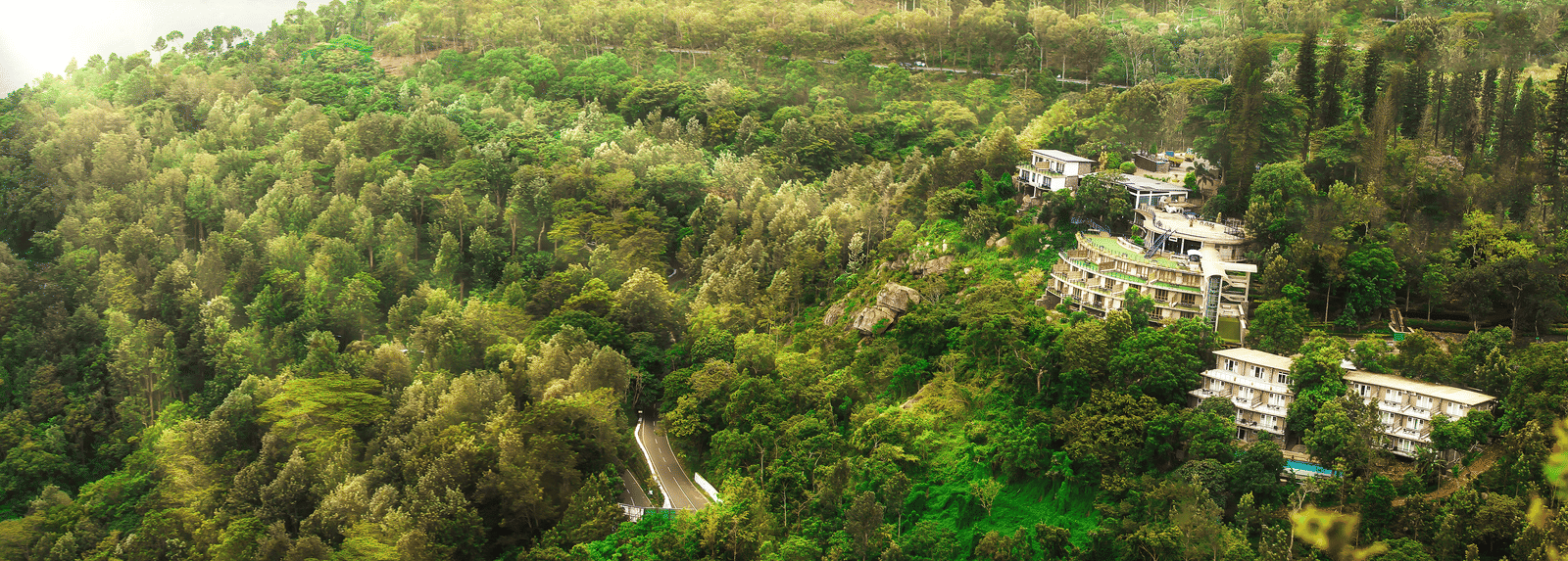 Drone shot of the hotel surrounded by mountains with sun light hitting the lush greenery - Great Trails Yercaud by GRT Hotels