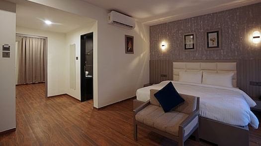 Spacious room at Grand Continent, Anjuna featuring a large bed, a sofa, dark curtains, decorative wall lights, and an open doorway.