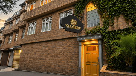 Exterior facade of Valmere Thistle Boutique Hotel, Darjeeling at dusk with a stone facade, ivy-covered wall, hanging signboard, and yellow door.