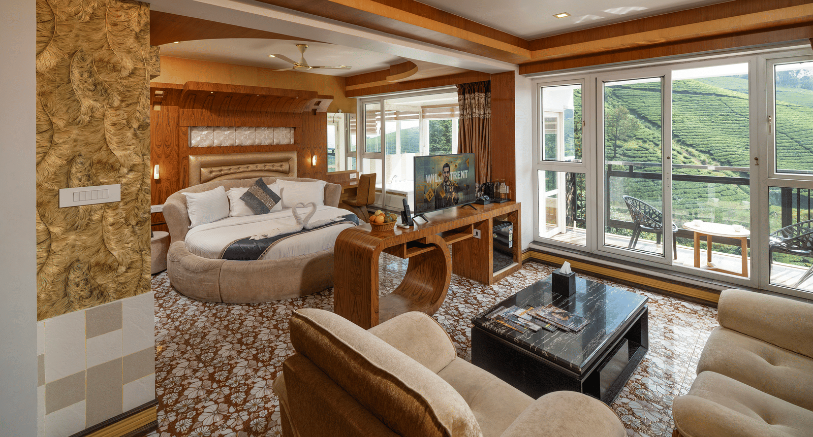 A living area of the Honey Moon Suite at Parakkat Nature Hotel and Resorts, Munnar, featuring plush seating, wood-panelled accents, an opening towards bedroom, and large windows offering a view of the landscape.