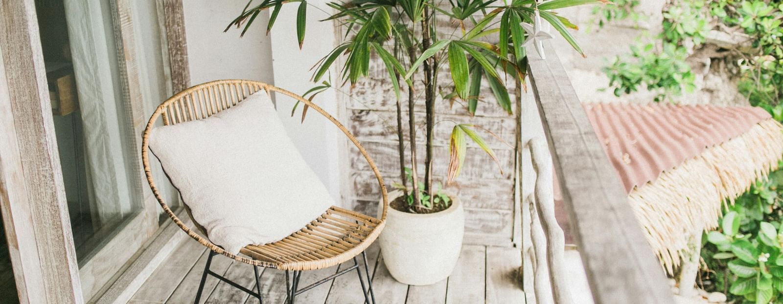 Balcony with a rattan chair, white cushion, potted plant, wooden floor, and railing.