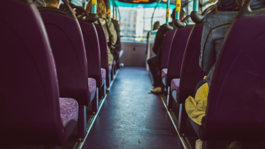 Interior of a public transport bus with purple seats and passengers seated, viewed down the aisle towards the front windscreen and overhead handrails.