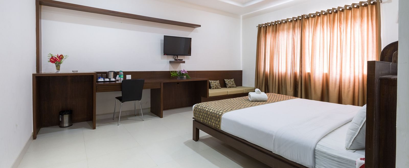 A well-lit room with a bed, desk area, television, and curtains - Sanctum Suites BEL Road, Bangalore