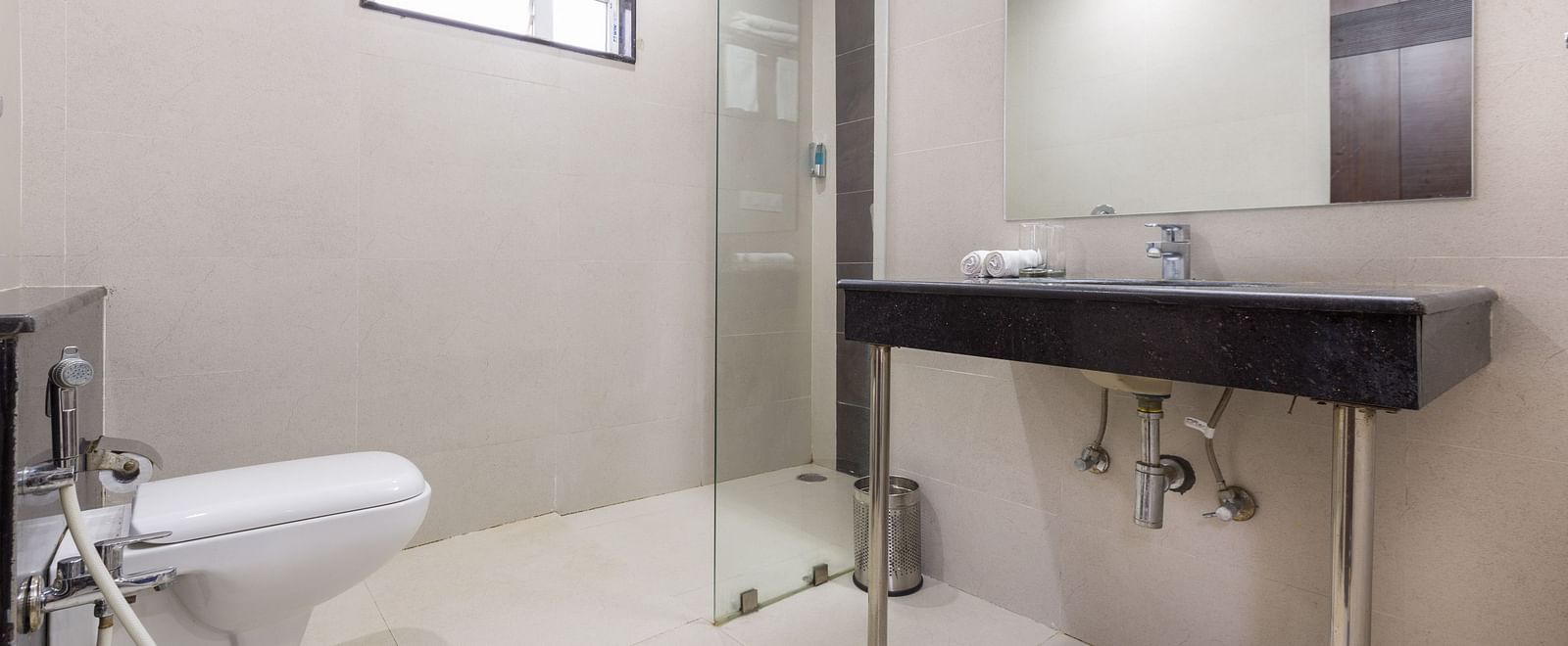 A modern bathroom with a dark counter top sink, toilet, and glass shower enclosure - Sanctum Suites BEL Road, Bangalore