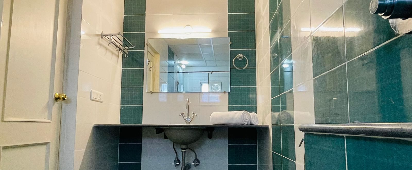 A bathroom featuring teal and white tiling and a sleek washbasin with a mirror at Sanctum Suites Indiranagar, Bangalore.