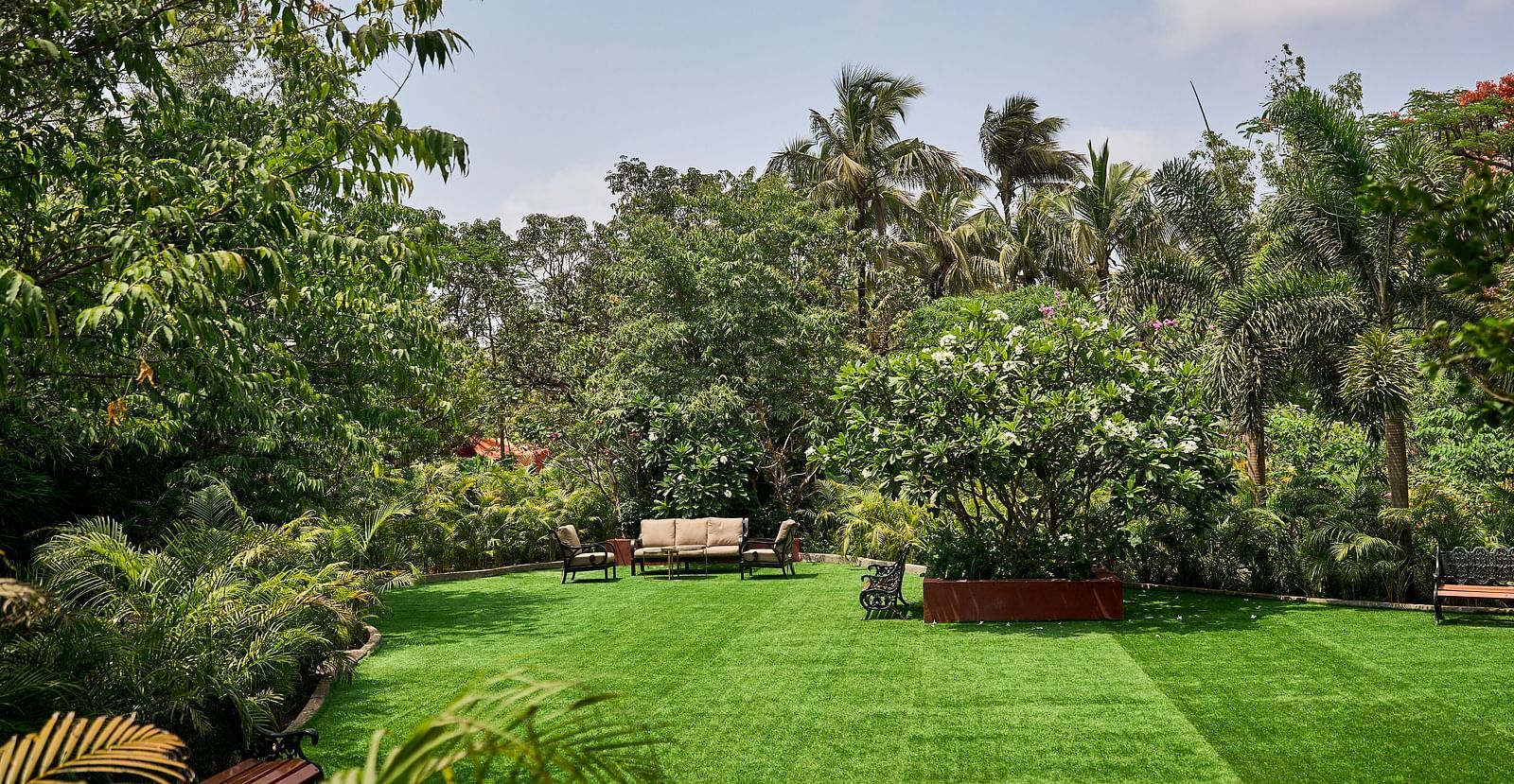 Lawn area encircled by trees and plants, with seating arranged for relaxation at Mayfair Manor, Alibag
