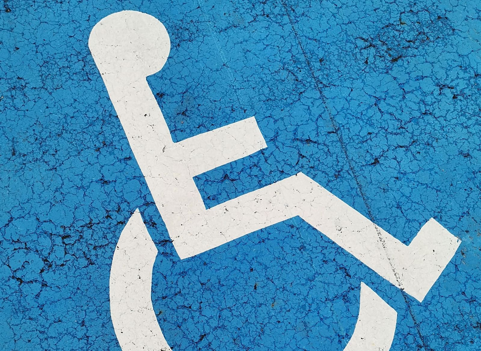 A straight-on, eye-level shot of a blue asphalt parking space with a white painted wheelchair symbol in the center. 