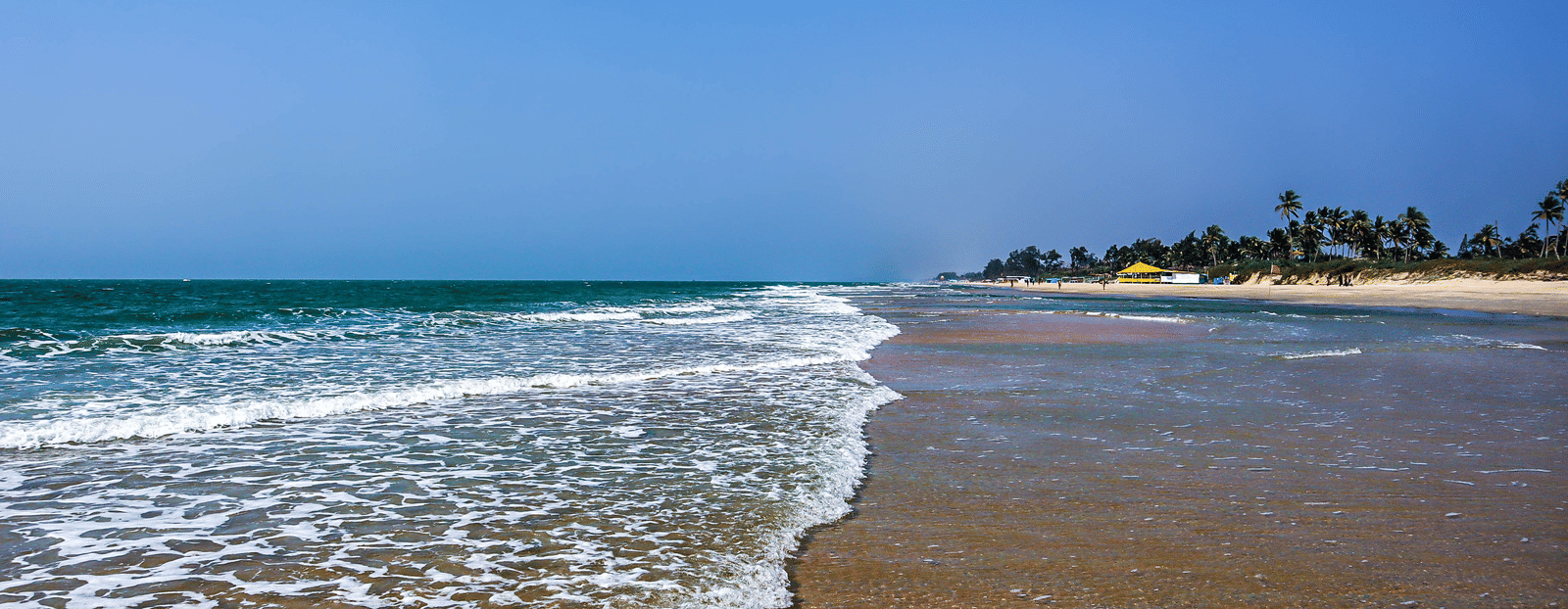 Foamy Waves flowing over the sand at varca beach with beach umbrellas in the background