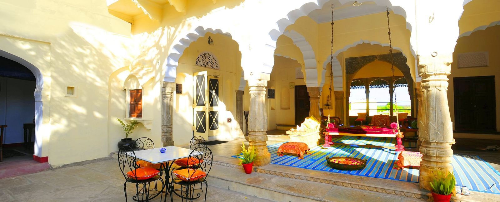 A sun-drenched courtyard at Fort Barli, with arched colonnades and a swing, offers a charming blend of architecture and relaxation.