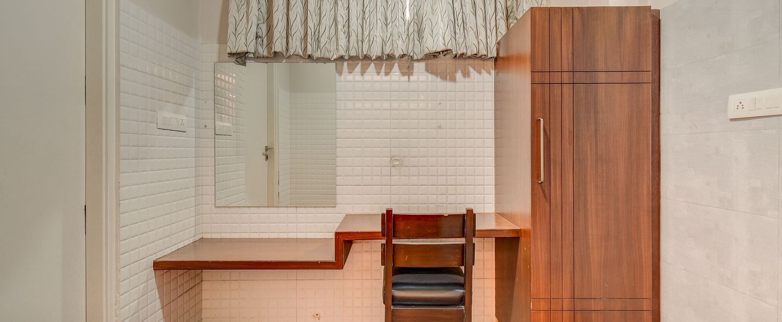 A wooden wardrobe at Harigovinda's JNStay with a desk placed next to it and a wooden chair