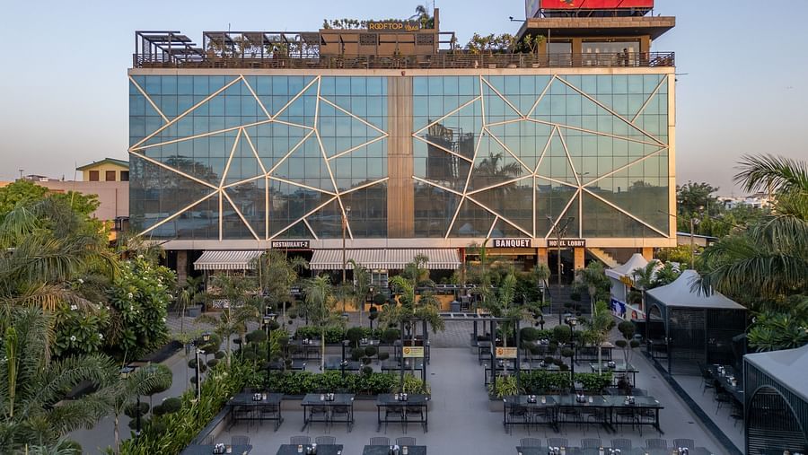 Exterior view of Hotel Highway King, Jaipur, with a large glass facade and rooftop signage, surrounded by greenery.
