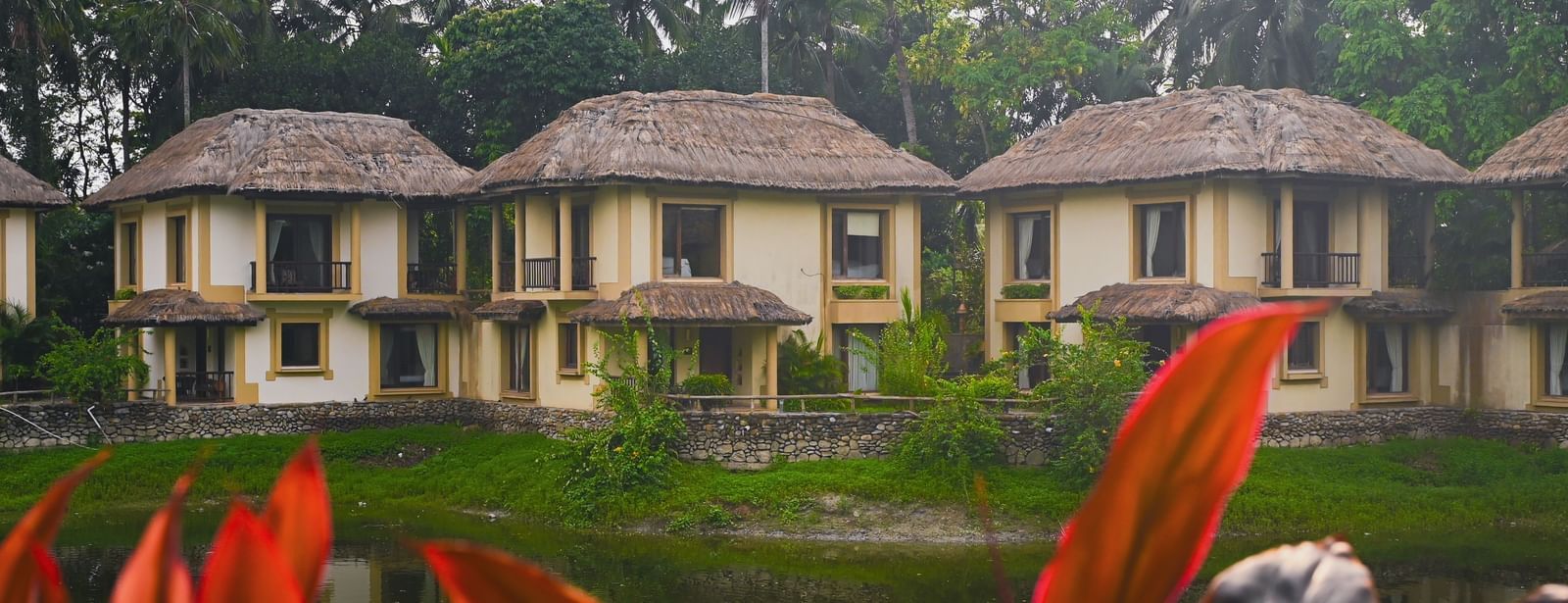 Row of thatched-roof Lake View Villas at Vedic Village Spa Resort with balconies facing the lake and ducks swimming in the water.
