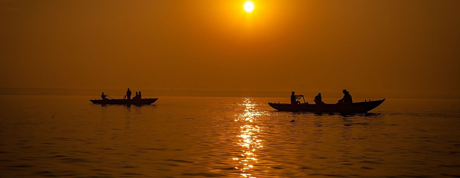A sunset image of Varanasi, showcasing two boats with a few people in them.