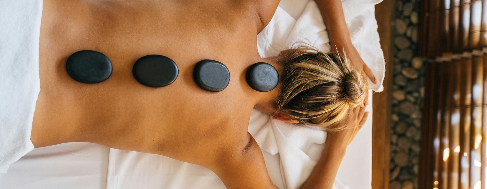 A woman lying down with back with black stones kept over her spine.