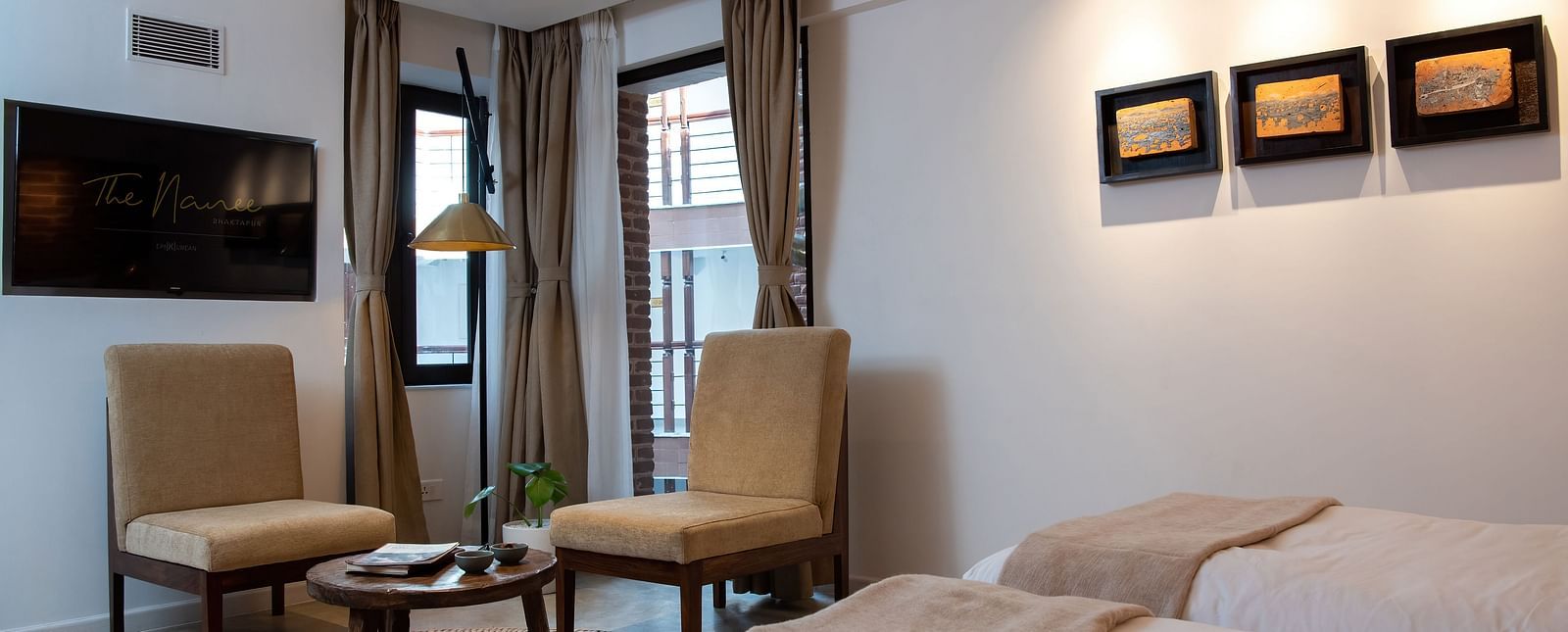 A room with a bed, chairs, table, flat screen TV, and three artwork hung on the wall - The Nanee