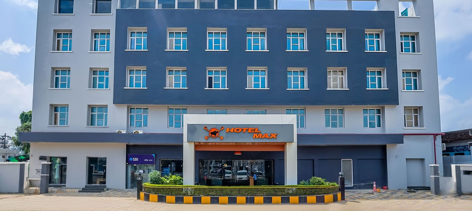 A front view of a hotel building with the name of the hotel mentioned on a signage - Max Hotel Prayagraj