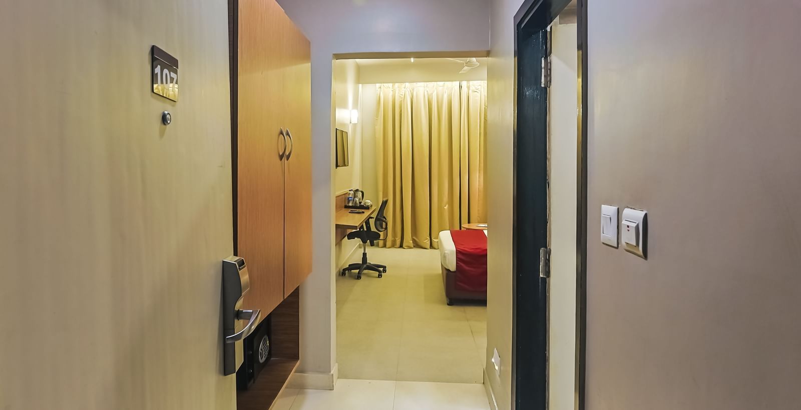 Bedroom entrance view with bed, curtains and wall-mounted TV at Max Hotel Prayagraj.
