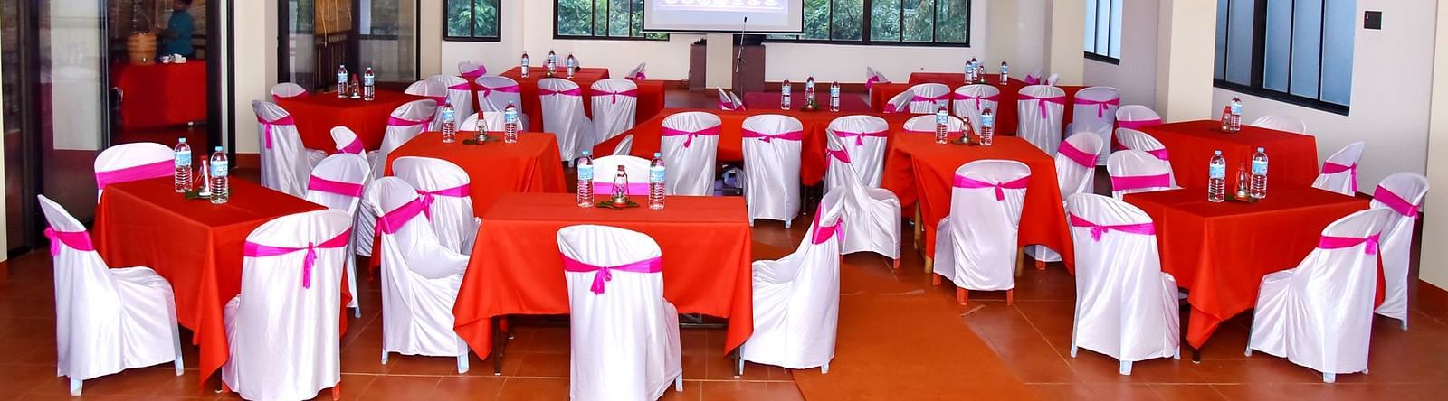 A banquet hall at Forest Escapes Koyna is elegantly set up with draped chairs and round tables, possibly for an event.