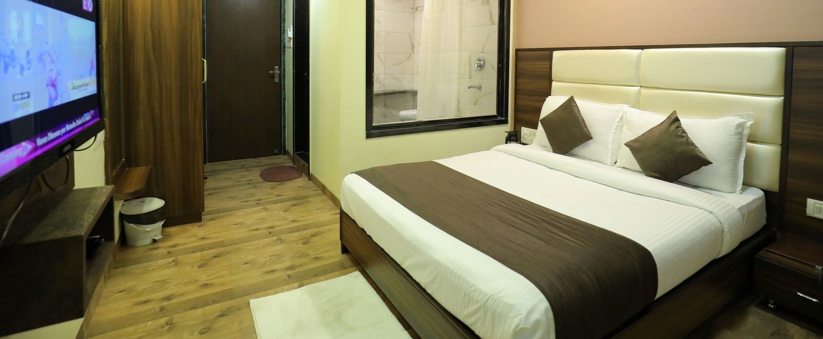 A bedroom at Krushnai Resort with a large TV, a king size bed, and a partial view of the bathroom through a glass wall.