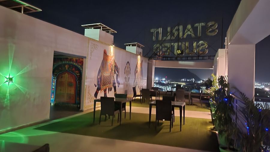 Outdoor rooftop dining at Starlit Suites, Neemrana, at night. Features green turf, tables, elephant mural, and city lights in background.