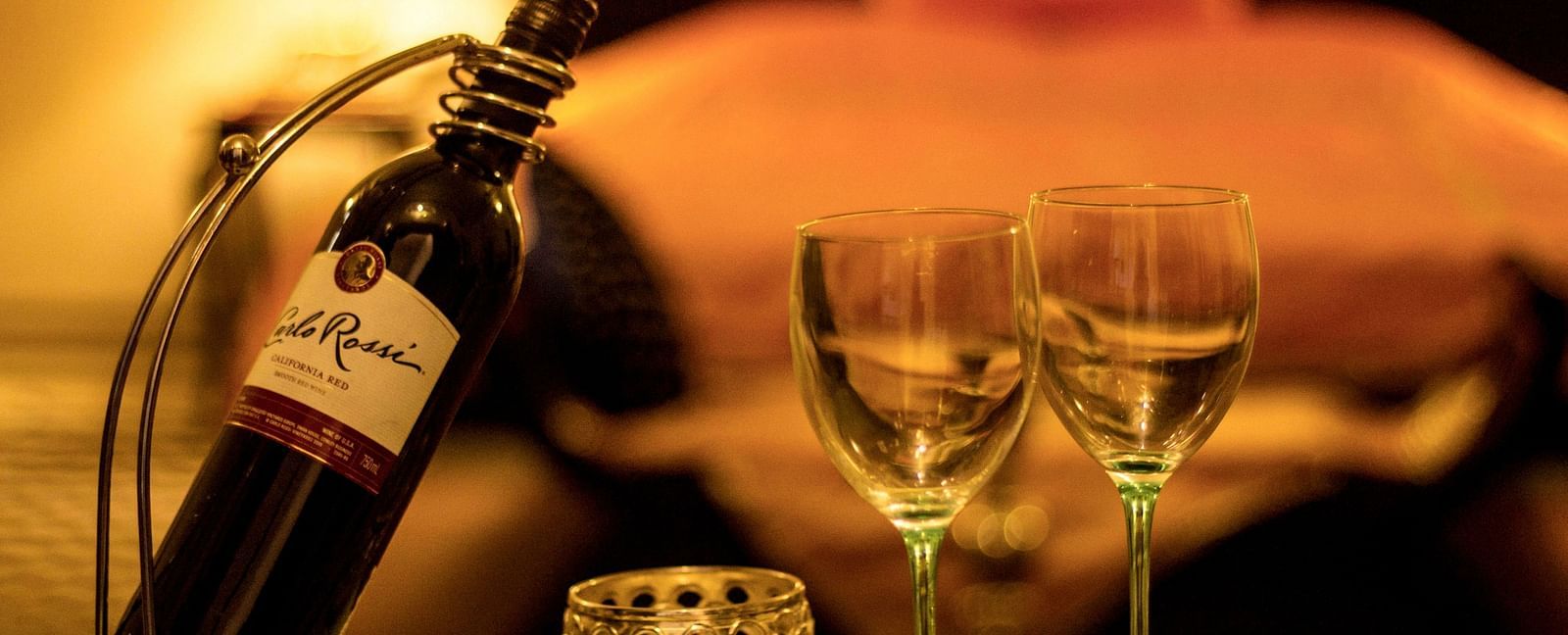 A bottle of wine and two glasses set on a table at Umaid Vilas Jaipur, with a blurred background suggesting a room setting.