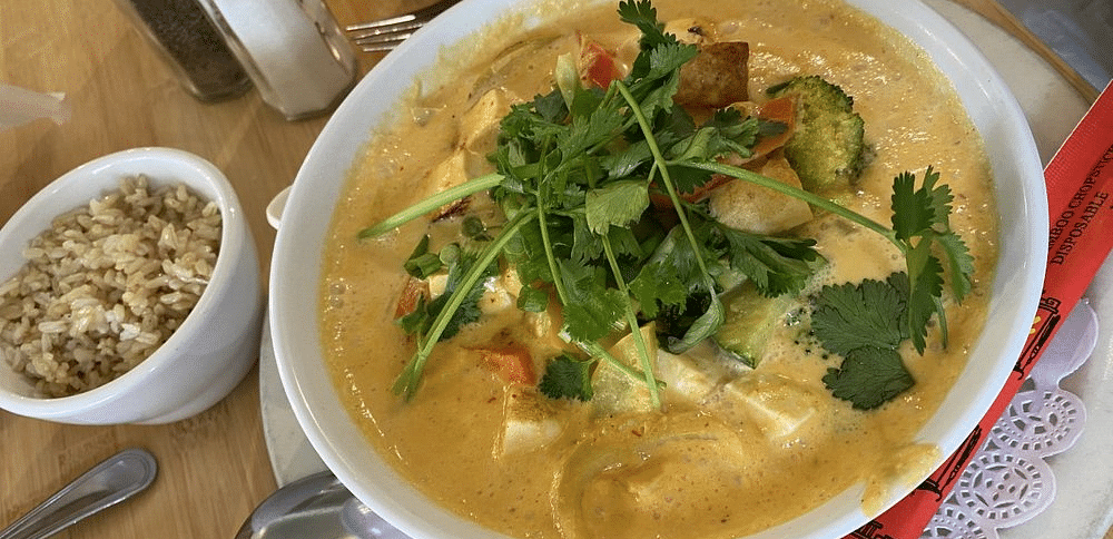 A bowl of soup with leafy greens and other ingredients, served with a spoon and small bowls of garnishes.