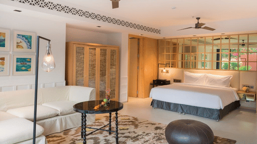 Room with a brown pouffe and a coffee table surrounded by a white couch in front of a plush bed at Azaya Beach Resort Goa