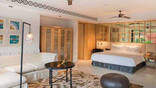 Room with a brown pouffe and black round table surrounded by a white couch and bed