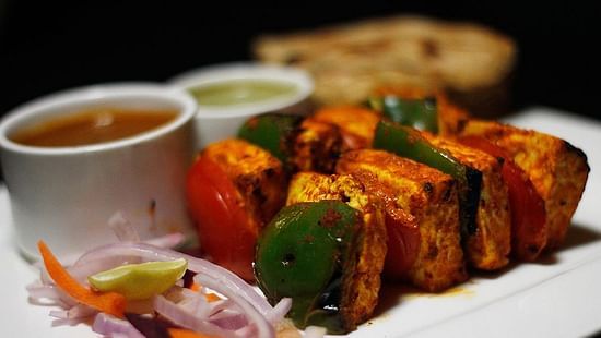 Paneer Tikka plated in a white dish with red and green chutney