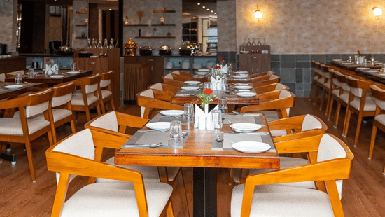 Well-arranged dining tables in Aromas restaurant at VITS Select, Bengaluru, with neat place settings and warm wooden interiors in full view.